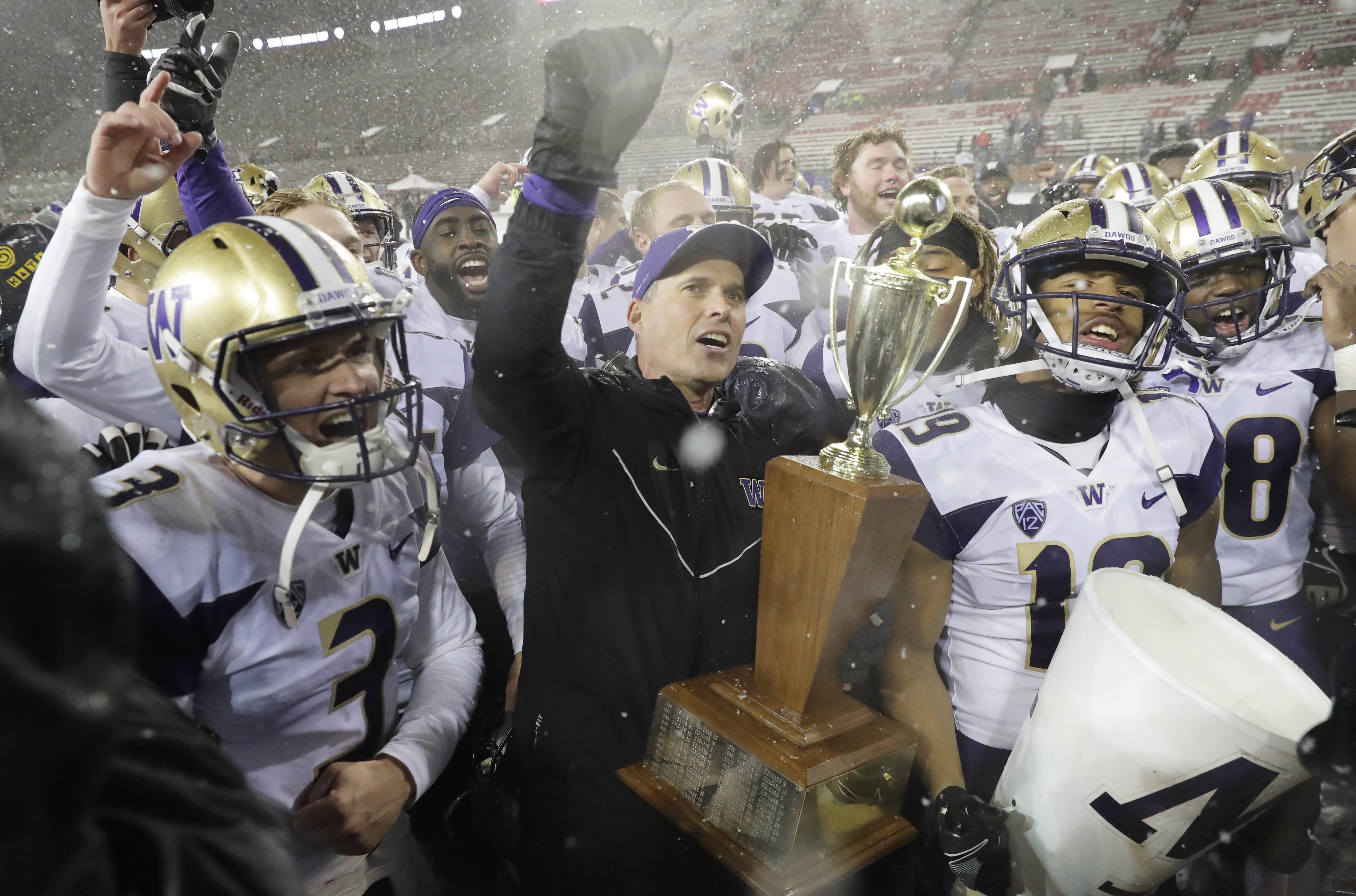 Washington coach Chris Petersen, center, holds the Apple Cup trophy as he celebrates with quarterback Jake Browning, left, and the rest of the team after Washington defeated Washington State 28-15 in an NCAA college football game Friday, Nov. 23, 2018, in Pullman, Wash. (AP Photo/Ted S.