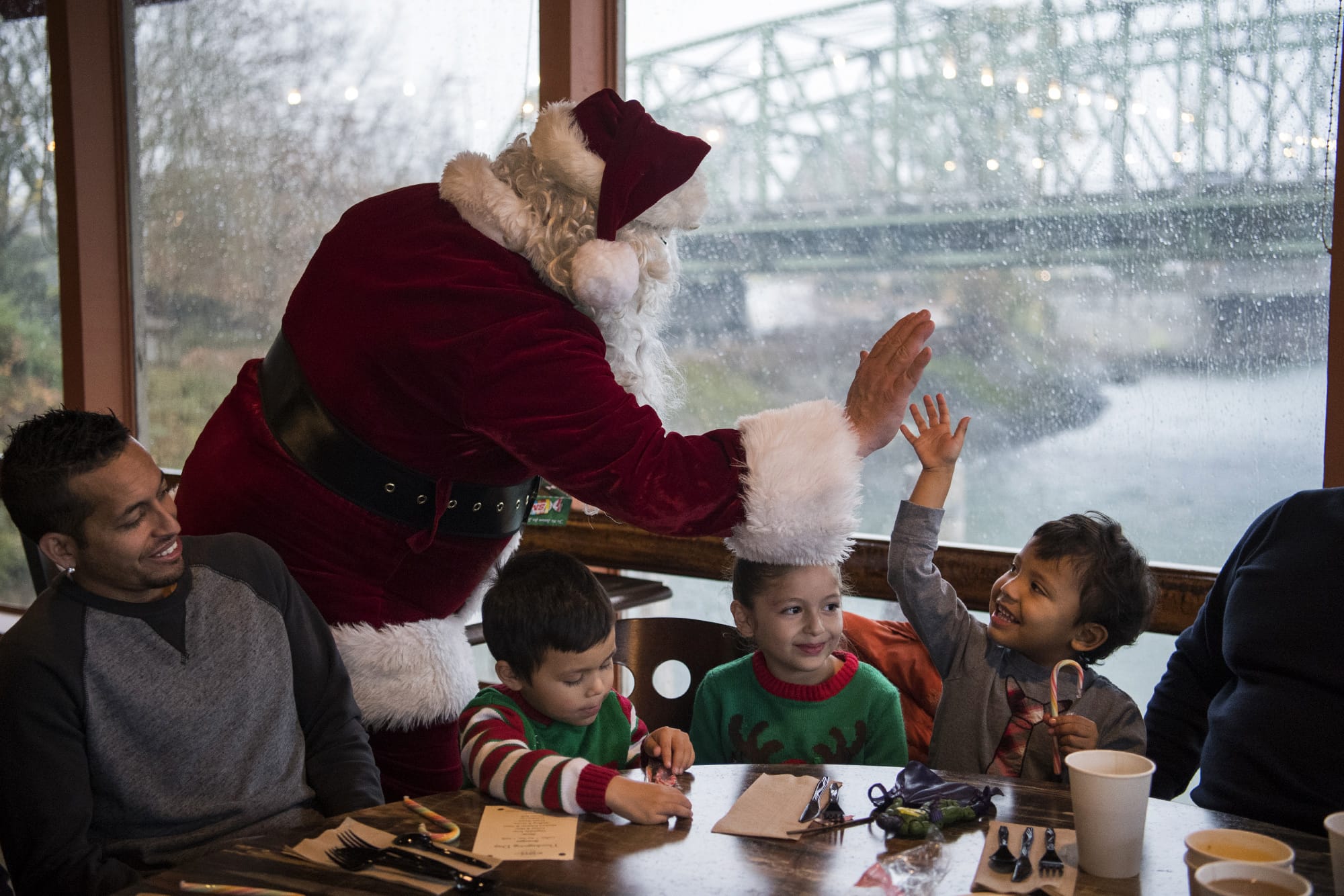 Dressed as Santa, Vince Hochanadel high-fives Rodrigo Solis, 3, at the free Thanksgiving meal at WareHouse '23 in Vancouver last month. Solis' cousins Emily Reseadiz, 6, center, Daniel Reseadiz, 3, center left, and Solis's uncle Victor Gonzalez, left, sit beside him. The meal was hosted by state Court of Appeals Judge Rich Melnick, Chuck Chronis and Mark Matthias.