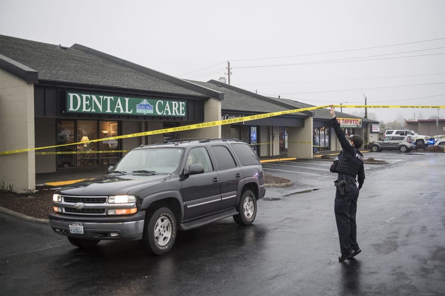 A Vancouver police officer lifts crime scene tape to allow a vehicle to leave the scene of a fatal shooting Monday afternoon at Pacific 63 Center in Hazel Dell.