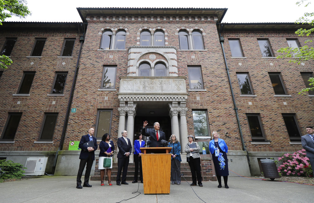 File - In this May 11, 2018 file photo, Washington Gov. Jay Inslee, center, speaks in front of Western State Hospital in Lakewood, Wash. Gov. Inslee unveiled Tuesday, Jan. 11, 2018, his budget and policy plan for fixing the state's struggling mental health system in the coming years. Inslee said he wanted to invest in the troubled Western State Hospital to address safety concerns there, but he didn't mention the rise in assaults at the state's largest psychiatric hospital. (AP Photo/Ted S.