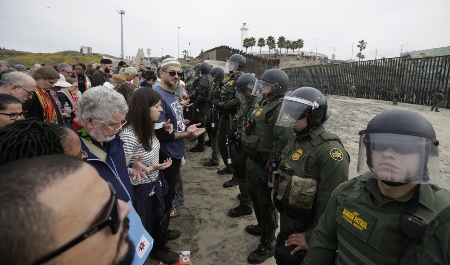 Immigrant rights activists stand arm in arm and line up against border patrol agents Monday during a protest at the border wall in San Diego.