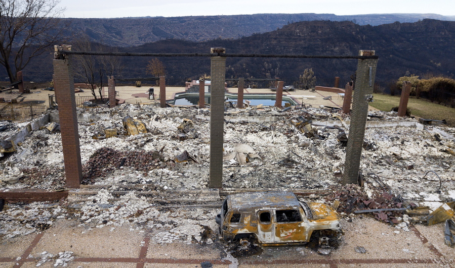 FILE - In this Dec. 3, 2018 file photo, a vehicle rests in front of a home leveled by the Camp Fire in Paradise, Calif. Authorities estimate it will cost at least $3 billion to clear debris of 19,000 homes destroyed by California wildfires last month. State and federal disaster relief officials said Tuesday, Dec. 11, 2018, that private contractors will most likely begin removing debris in January from Butte, Ventura and Los Angeles counties and costs are likely to surpass initial estimates.
