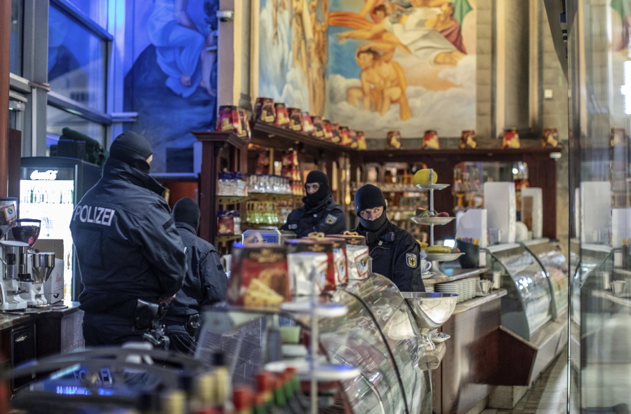 Masked police stand in an ice parlor in Duisburg, western Germany, Wednesday, Dec. 5, 2018 as authorities conduct coordinated raids in Germany, Italy, Belgium and the Netherlands in a crackdown on the Italian mafia.