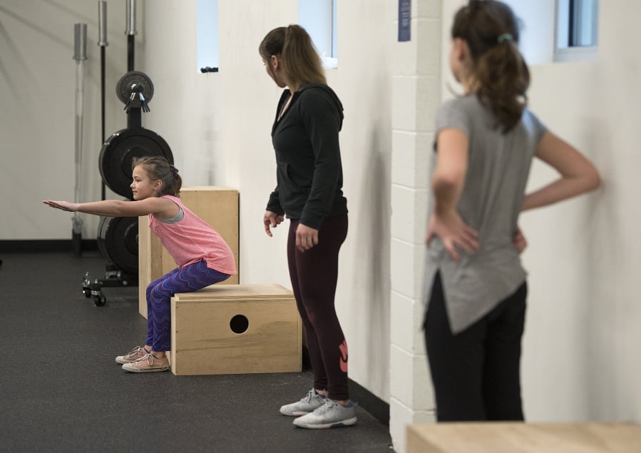 Richelle Endres, 10, of La Center, from left, squats during a Fit Kids class with instructor Kelsey Walsh and Aeryn Knowles, 11, of Vancouver, , at Salmon Creek Bridge Chiropractic. “I want to make them fall in love with what they’re doing,” Walsh said of her goal for the class.