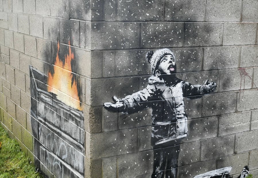 FILE - In this file photo dated Dec, 20, 2018, showing an artwork by Banksy on the side of a garage depicts a child dressed for snow playing in the falling ash and smoke from a skip fire, in Port Talbot, Wales. The artwork has been sold to an Essex art dealer for a “six-figure sum”, although the mural will stay in its current location for about two-years, it is revealed Friday Jan. 18, 2019.