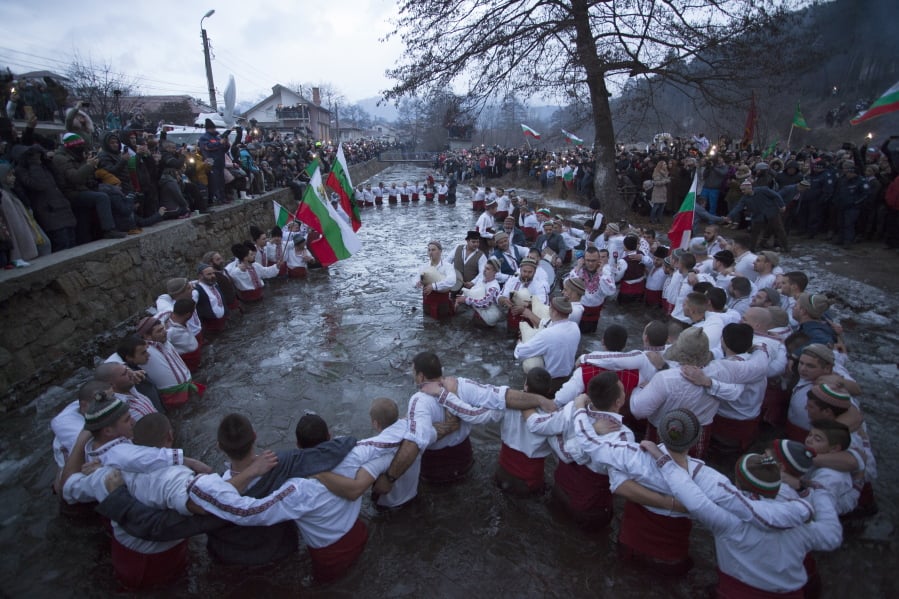 Bulgarians sing and chaindance in the icy waters of the Tundzha river in Kalofer, Bulgaria, Sunday, Jan. 6, 2019. Traditionally, an Eastern Orthodox priest throws a wooden cross in the river and it is believed that the one who retrieves it will be healthy through the year. In the mountain city of Kalofer, in central Bulgaria, dozens of men dressed in white embroidered shirts waded into the frigid Tundzha River waving national flags and singing folk songs.