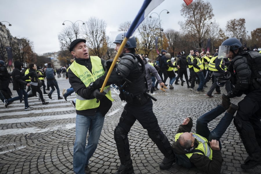 FILE - In this Saturday, Nov. 24, 2018 file photo, Herve Ryssen, left, close to the ultra-right and convicted for antisemitic and racist comments, wearing a yellow jacket, clashes with riot police officers on the Champs-Elysees avenue in Paris. Intolerance and conspiracy theories have haunted the margins of France’s “yellow vest” movement since the first protests over fuel taxes roused the discontented middle of French society.