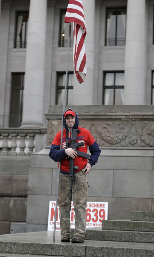 Micheal Thompson wears a shirt and hat supporting President Donald Trump as he holds a an AR-15 rifle and a U.S. flag while taking part in a gun-rights rally, Friday, Jan. 18, 2019, at the Capitol in Olympia, Wash. (AP Photo/Ted S.