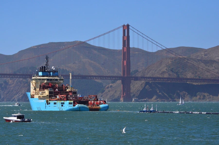 FILE- In this Sept. 8, 2018 file photo, a ship tows The Ocean Cleanup’s first buoyant trash-collecting device toward the Golden Gate Bridge in San Francisco en route to the Pacific Ocean. A trash collection device deployed to corral plastic litter floating between California and Hawaii will be hauled back to dry land for repairs. Boyan Slat, who launched the Pacific Ocean cleanup project, tells NBC the 2,000-foot (600-meter) long floating boom will be towed to Hawaii. If it can’t be repaired there it will be loaded on a barge and returned to its home port of Alameda, Calif. The boom broke apart under constant wind and waves. Slat says he’s disappointed, but not discouraged.