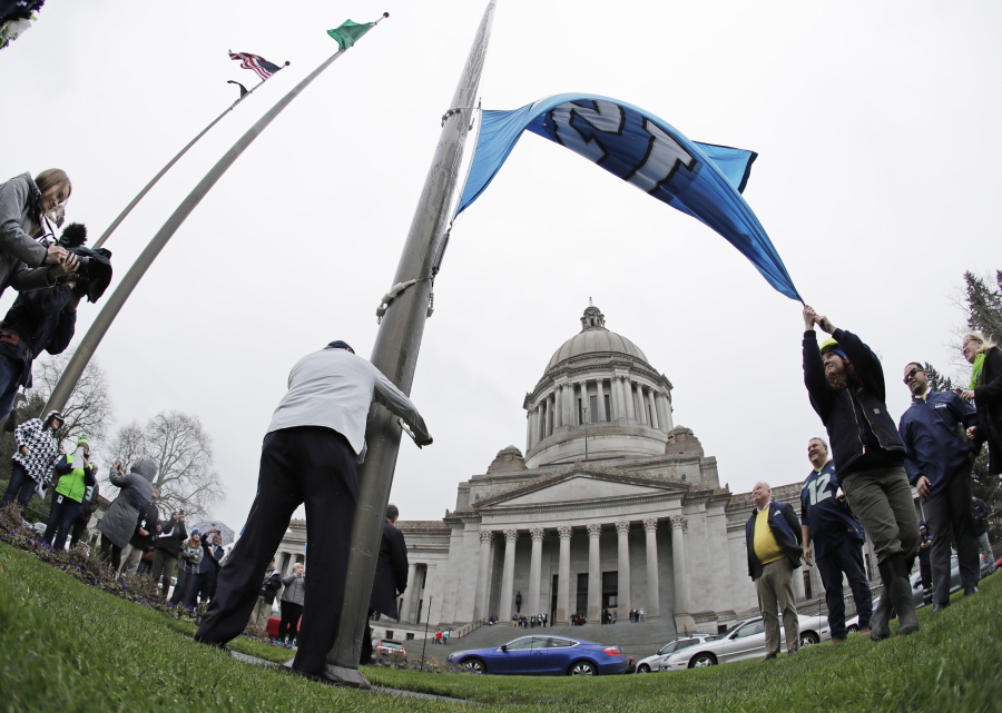 Washington Gov. Jay Inslee, center-left, turns a crank to raise a Seattle Seahawks 12 flag, Thursday at the Capitol in Olympia. The Seahawks will play the Dallas Cowboys Saturday in an NFL football wild-card playoff game. Ted S.
