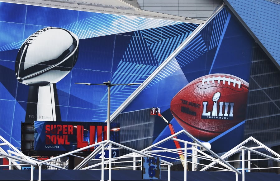 In this Jan. 17, 2019 photo, workers use a lift to install a Super Bowl 53 wrap on the outside of Mercedes-Benz Stadium as it is transformed for the big NFL football game in Atlanta. Kraft Heinz’ frozen-food brand Devour is trying to make waves during its Super Bowl debut with an ad taking a humorous jab at one man’s “frozen food porn addiction.” Super Bowl ads have long used raunchiness and sex stand out during the Super Bowl, advertising’s biggest stage. But the approach runs the risk of offending the audience.