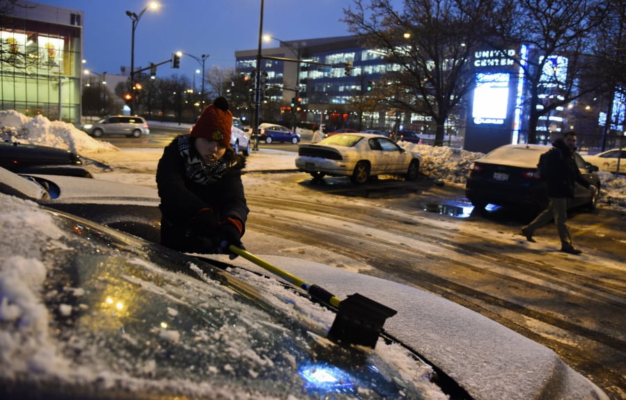 Meredith Davis scrapes off her car as snow and freezing rain arrived on Tuesday, Jan. 22, 2019, in Chicago.