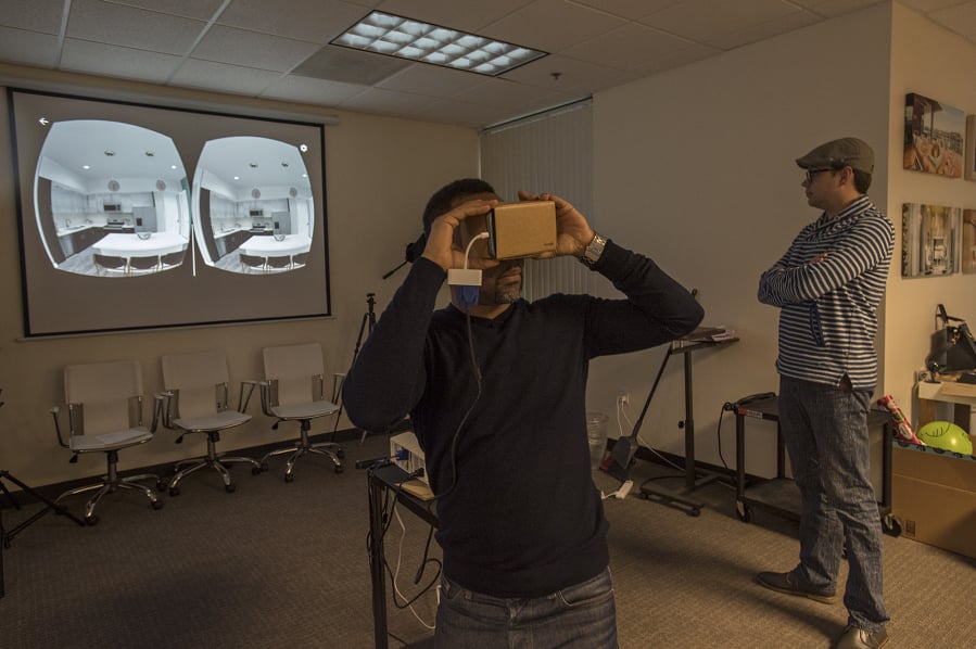 Barrie Buckner, GTMA director of partnerships, center, views an apartment in virtual reality using his smartphone while CEO Joshua Swanson watches. The image on the projector screen shows what Buckner is seeing; each eye views one of the two images, creating what the viewer perceives as a single three-dimensional view.