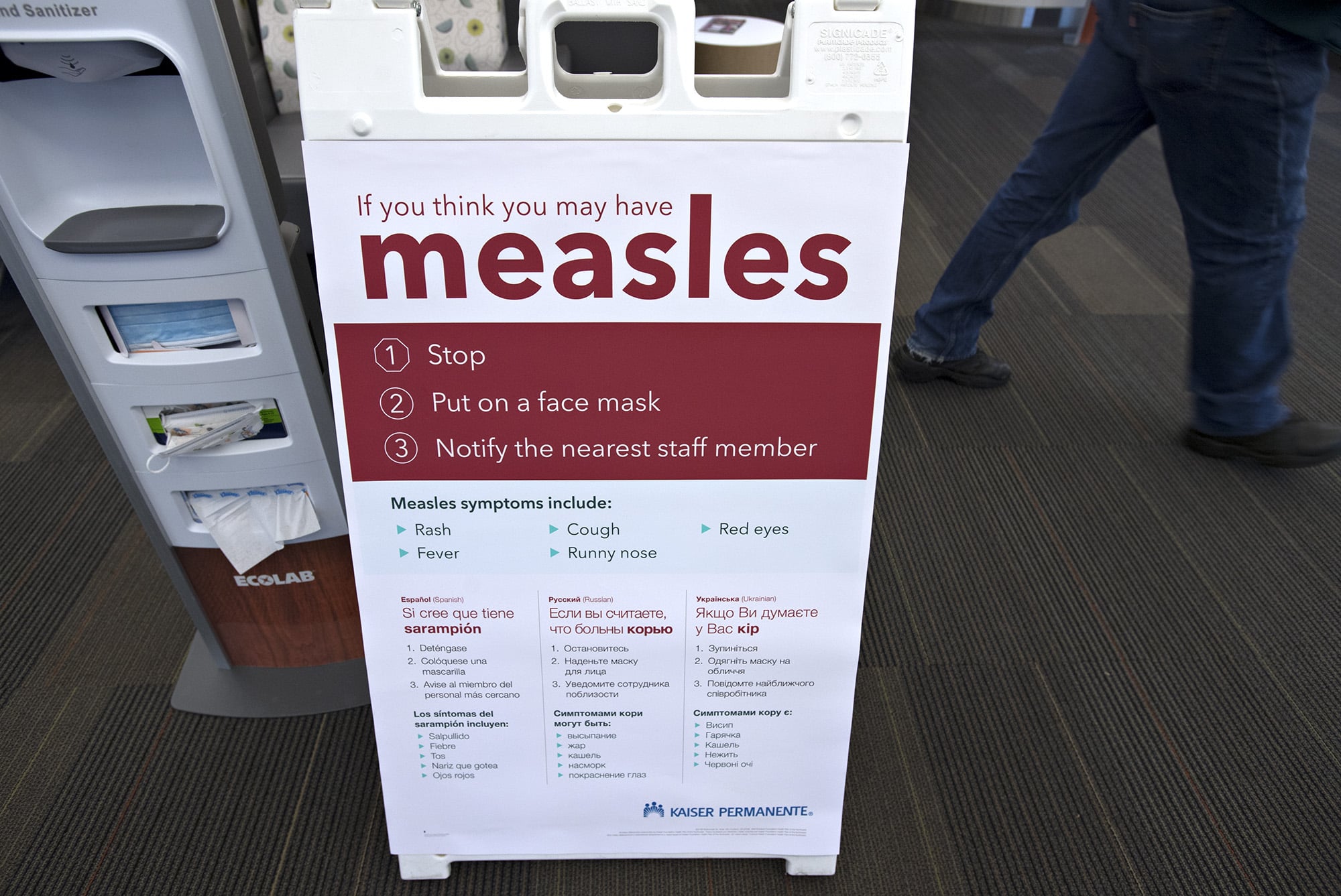 A pedestrian walks past an informational sign about the measles in the entrance of the Kaiser Permanente Cascade Park office Monday morning, Feb. 4, 2019.