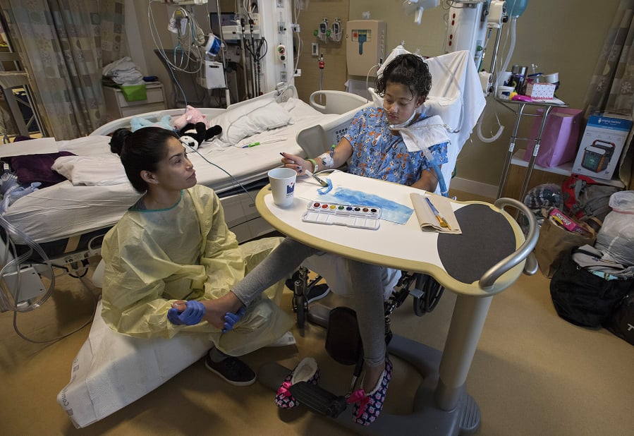 Physical therapist Janine Vizon, left, works on the feet of DejaRay Smith, 13, of Washougal as she also takes part in art therapy at Randall Children’s Hospital in Portland. DejaRay has been battling a MRSA infection for 59 days at Randall.