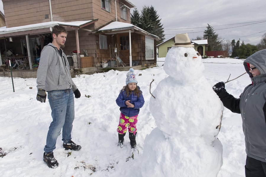 Terrance Crane, left, and Modesty Van Dusen, 5, watch neighbor Alex Cox, 10, add a stick arm to a snowman Sunday in Camas.
