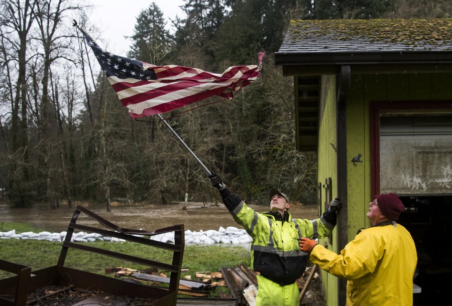 Ridgefield Public Works employee Nick Johnson, left, and James Barhitte, caretaker at Abrams Park in Ridgefield, move an American flag that was blocking a rain gutter on a park building Tuesday.