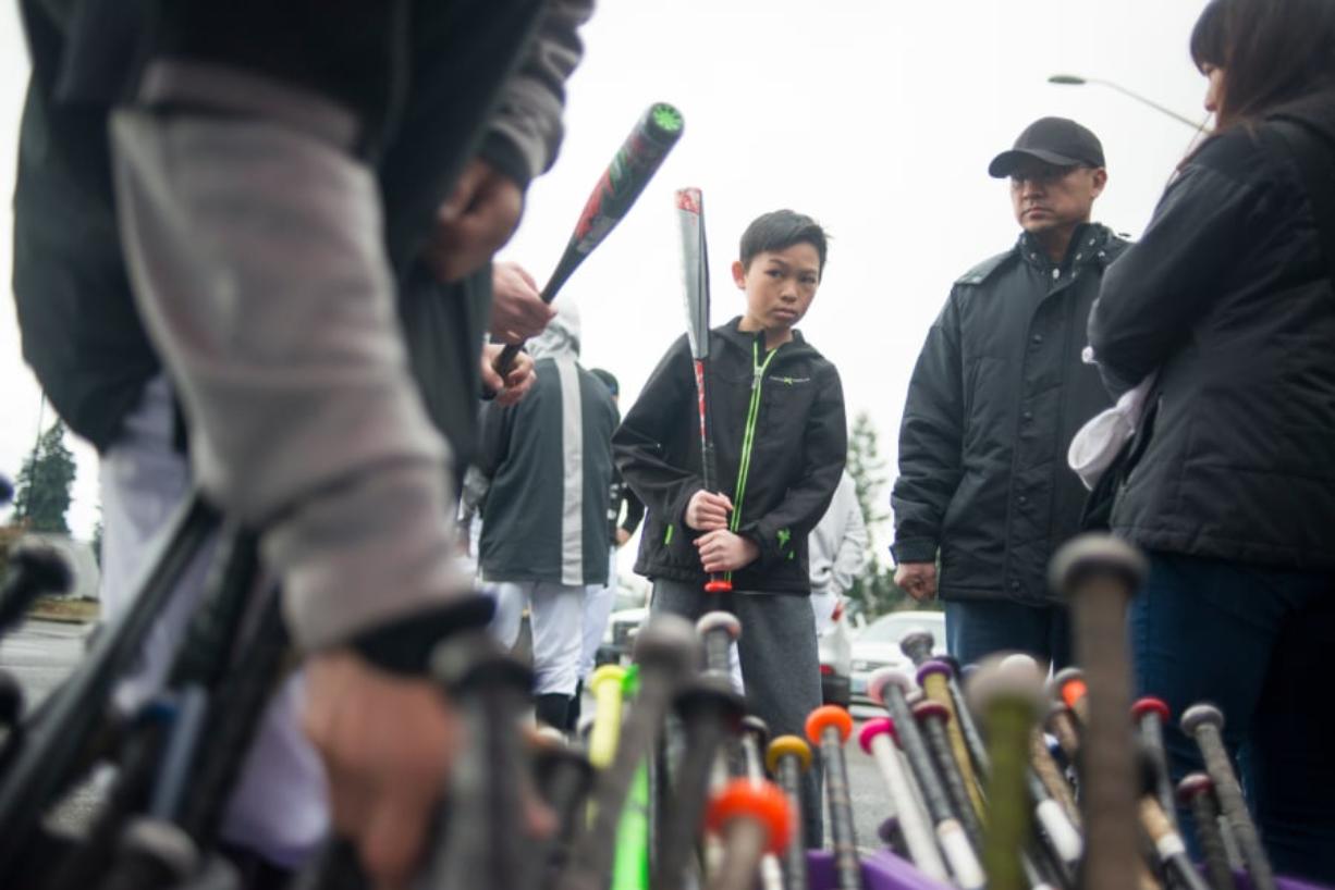 Ethan Le, 12, gets advice Sunday while picking out a baseball bat during a used baseball gear distribution event at Clark College. The event was organized by the Good Sport Equipment Connection and supported by groups including the Police Activities League.