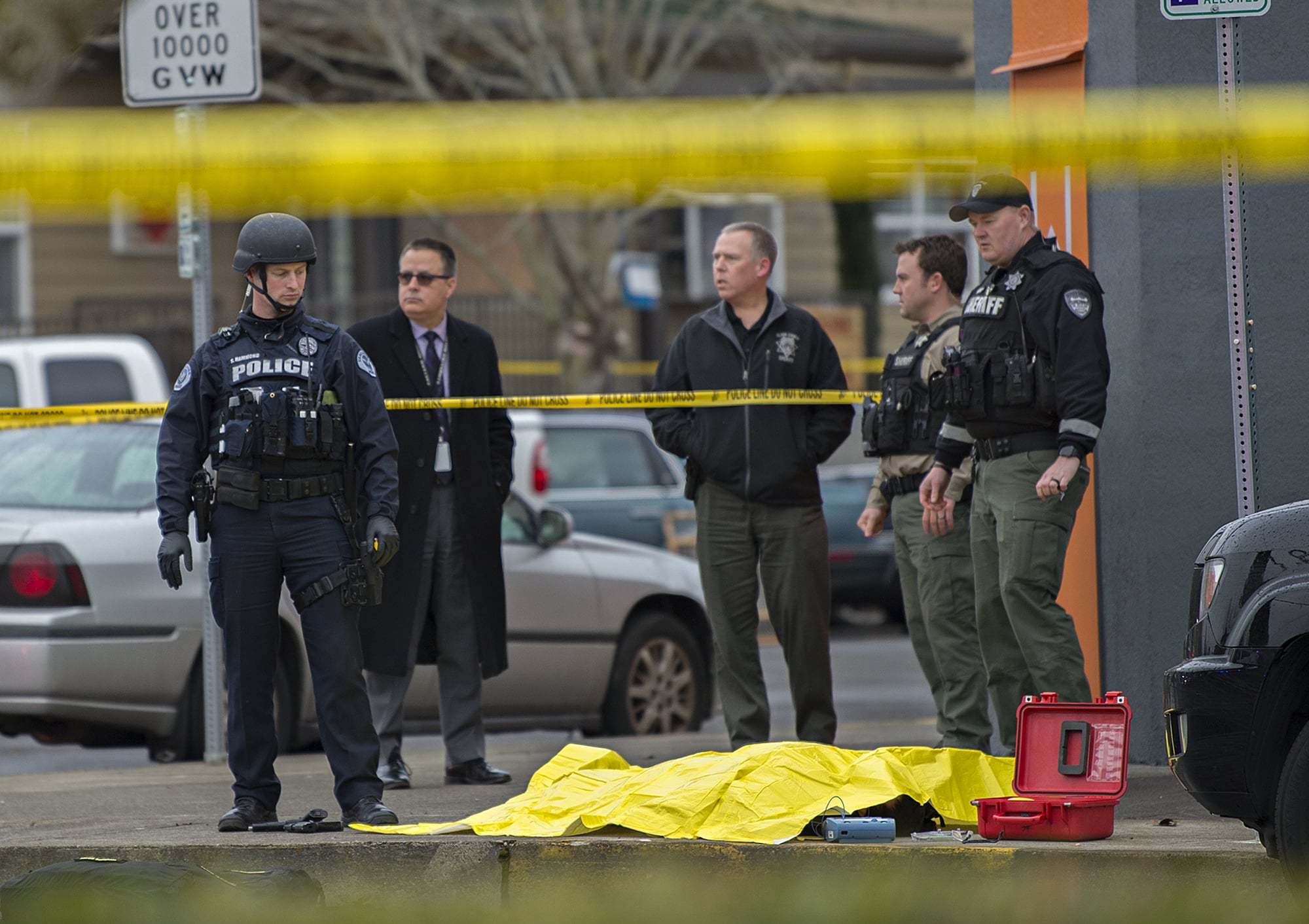 Vancouver police and Clark County Sheriff's deputies stand at the scene of a fatal officer-involved shooting at the corner of West 12th Street and Jefferson Street in downtown Vancouver on Thursday afternoon. The officer at the left appears to be standing over two firearms.