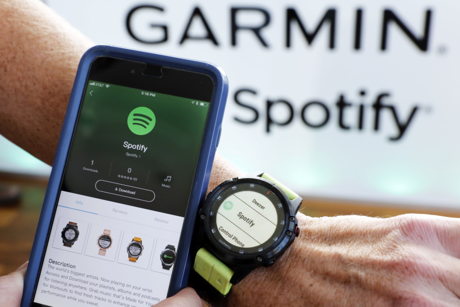FILE- In this Oct. 3, 2018, file photo a Garmin International employee shows the new Spotify app on his smartphone integrated with his Garmin fenix 5 Plus watch during a presentation in New York. Spotify reports financial results Wednesday, Feb. 6, 2019.