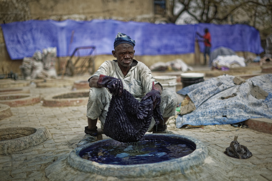 In this photo taken Tuesday, Feb. 19, 2019, a craftsman dyes cloth with indigo in one of the ancient dye pits of Kofar Mata in Kano, northern Nigeria. The dye pits were founded in 1498 and are said to be the last ones of their kind but some of the craftsmen grumble about competition from Chinese fabrics that have entered the markets and sell for half the price.