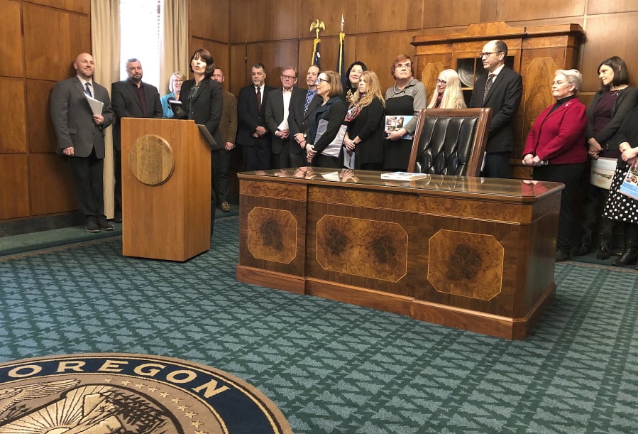 Margaret Salazar, director of Oregon Housing and Community Services, behind podium, speaks in front of Gov. Kate Brown, center left, at a news conference about a plan to attack homelessness in Salem, Ore., Monday, Feb. 11, 2019.