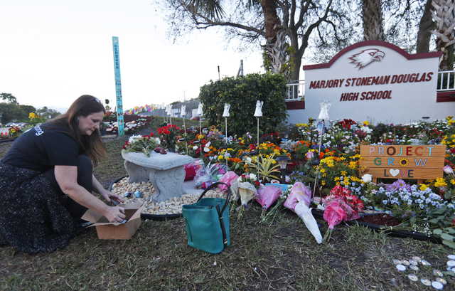 Suzanne Devine Clark, an art teacher at Deerfield Beach Elementary School, places painted stones at a memorial outside Marjory Stoneman Douglas High School during the one-year anniversary of the school shooting, Thursday, Feb. 14, 2019, in Parkland, Fla. A year ago on Thursday, 14 students and three staff members were killed when a gunman opened fire at the high school.