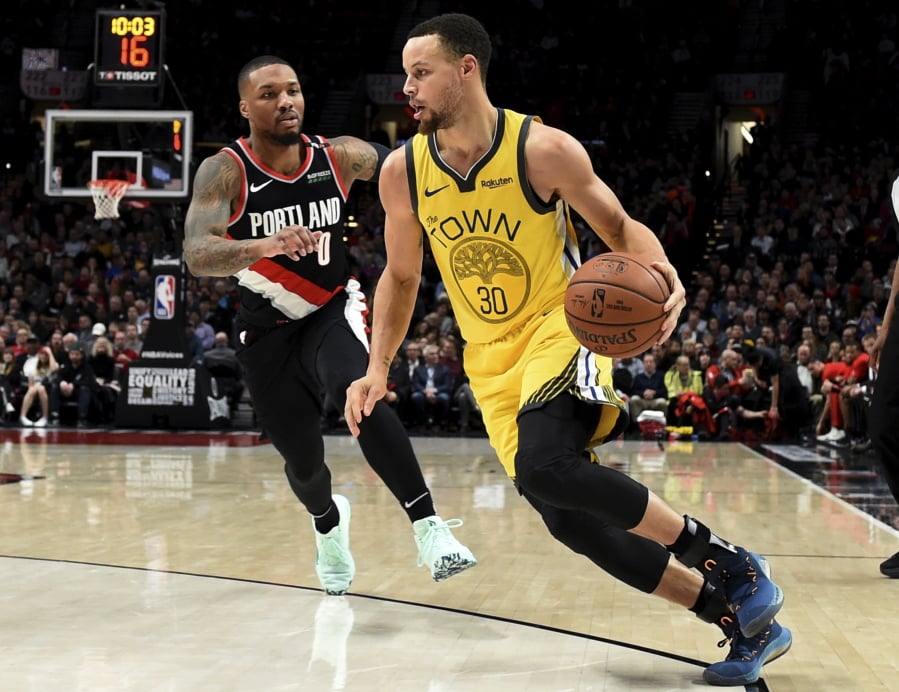 Golden State Warriors guard Stephen Curry, right, drives to the basket past Portland Trail Blazers guard Damian Lillard during the first half of an NBA basketball game in Portland, Ore., Wednesday, Feb. 13, 2019.