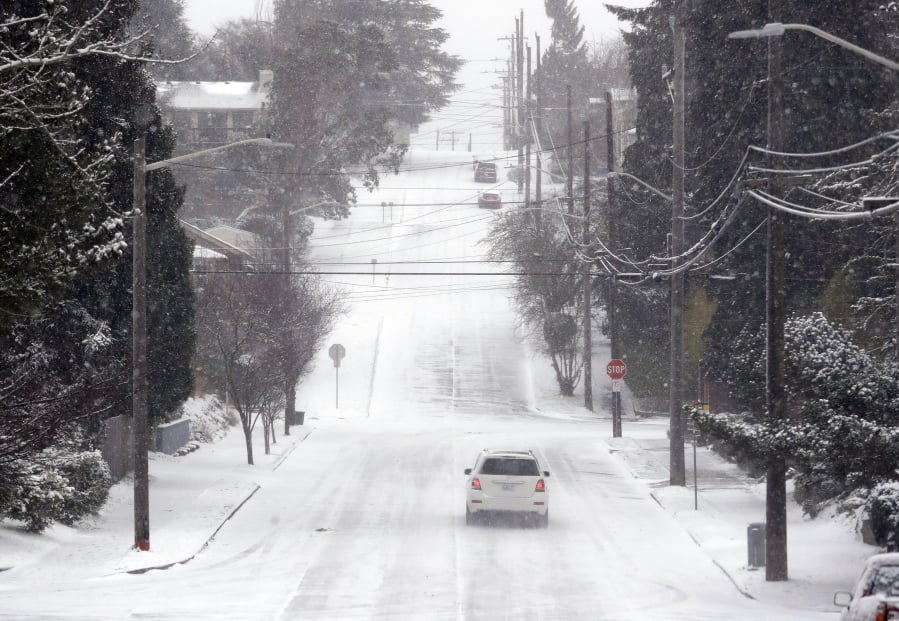 A lone car finds its way along an otherwise deserted street through snow and a cold wind Monday morning, Feb. 4, 2019, in Seattle. Western Washington was hit by a major winter storm, with several inches of snow, cold temperatures and bone-chilling winds overnight and into the day Monday. Numerous school districts have closed for the day and temperatures were in the low 20s across much of the region with wind chills in the teens.