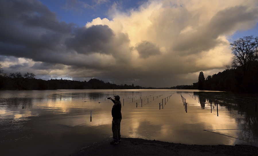 Aldo Cabrera, of Forestville, Calif., photographs the sunset at Wholer Road in Forestville, Calif., as the Russian River and Mark West Creek floods vineyards, Thursday, Feb. 14, 2019. Waves of heavy rain pounded California on Thursday, trapping people in floodwaters, washing away a mountain highway, triggering a mudslide that destroyed homes and forcing residents to flee communities scorched by wildfires last year.