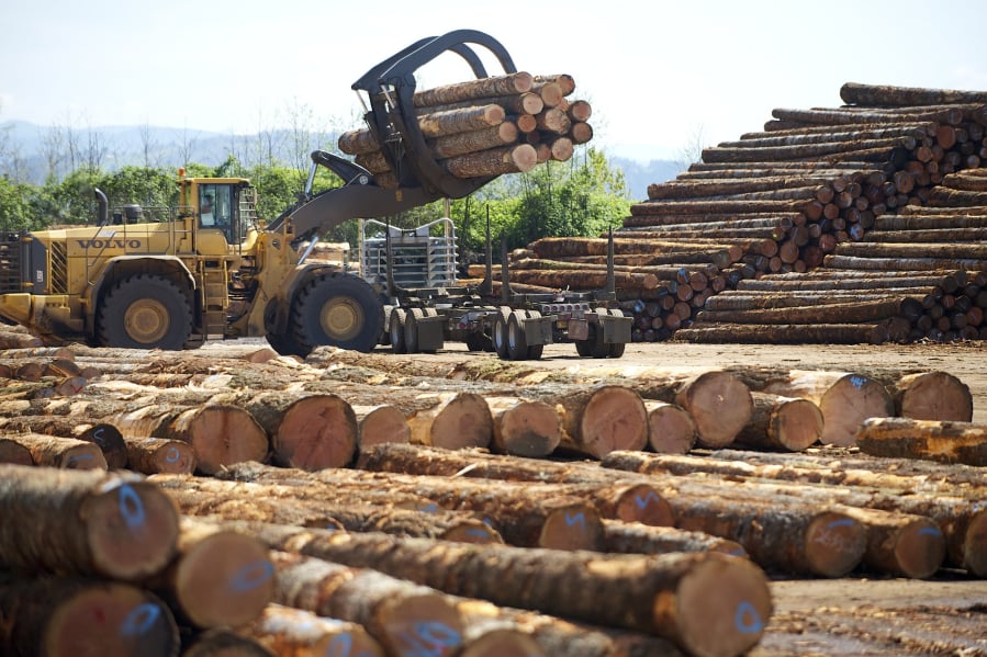 A log loader picks up a load of timber from a truck.