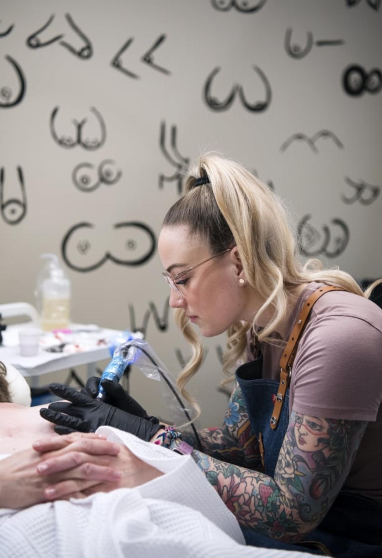 Vancouver resident Lina Anderson performs an areola restoration procedure with her client Mary, of Vancouver, at Studio Meraki in Portland. In the background, Anderson has a wall of breasts that she painted.