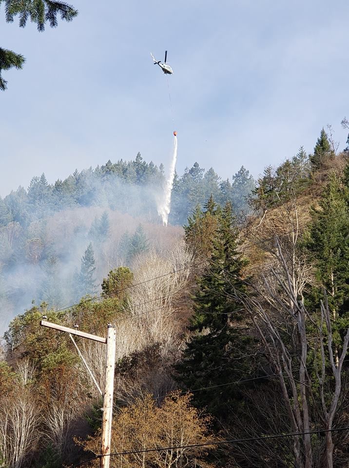 A state Department of Natural Resources helicopter drops water on a fire in eastern Wahkiakum County on Wednesday. The fire is bring on steep slopes right above State Route 4 but the highway remains open.