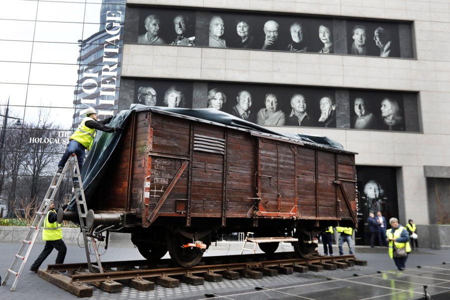 Portraits of Holocaust survivors are displayed at the Museum of Jewish Heritage as a vintage German train car, like those used to transport people to Auschwitz and other death camps, is uncovered on tracks outside the museum, in New York, Sunday, March 31, 2019. The train car joins hundreds of artifacts from Auschwitz at the museum for an exhibit entitled “Auschwitz. Not long ago. Not far away,” that opens to the public on May 8.