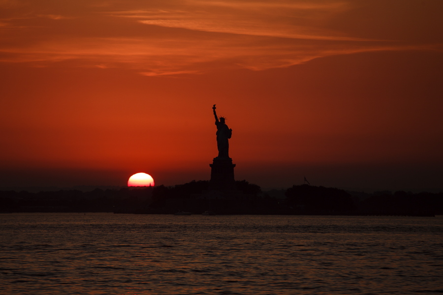 FILE - In this July 1, 2018 file photo, the sun sets behind the Statue of Liberty in New York as record high temperatures were recorded over the week in the U.S. and elsewhere. An AP data analysis of records from 1999-2019 shows that in weather stations across America, hot records are being set twice as often as cold ones.