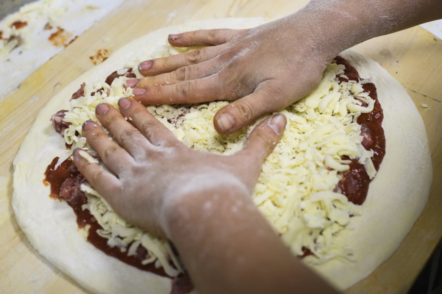 FILE - In this Sept. 26, 2018 file photo, a worker adds cheese to a raw pizza at a shop in Pittsburgh. A report released Tuesday, March 5, 2019 by the National Academies of Science ties the recommended limit on sodium to a reduced risk of chronic disease. Sodium can be hidden in bread, pizza, soup and an array of other foods.