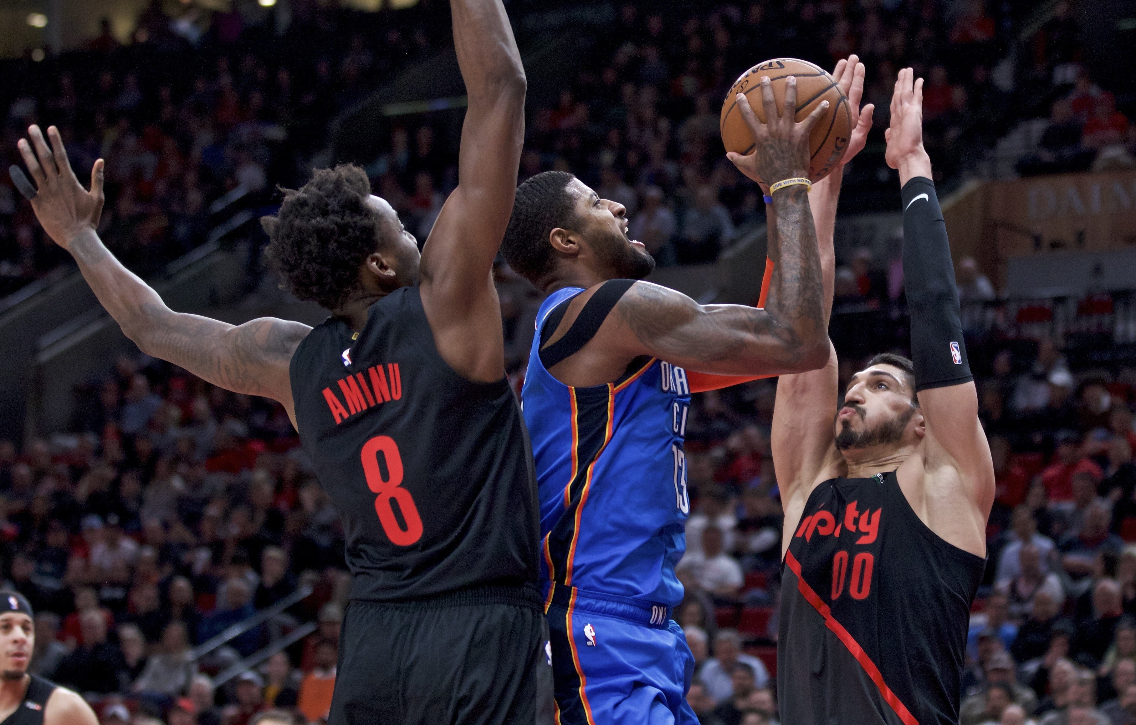 Oklahoma City Thunder forward Paul George, center, shoots between Portland Trail Blazers center Enes Kanter, right, and forward Al-Farouq Aminu during the first half of an NBA basketball game in Portland, Ore., Thursday, March 7, 2019.