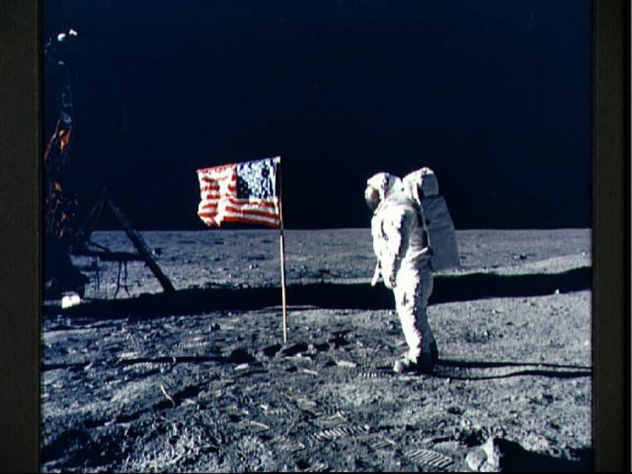 Astronaut Edwin E. Aldrin Jr., lunar module pilot, poses for a photograph beside the deployed United States flag during Apollo 11 extravehicular activity on the lunar surface. The Lunar Module “Eagle” is on the left. The footprints of the astronauts are clearly visible in the soil of the moon. This picture was taken by Astronaut Neil Armstrong, commander, with a 70mm lunar surface camera.