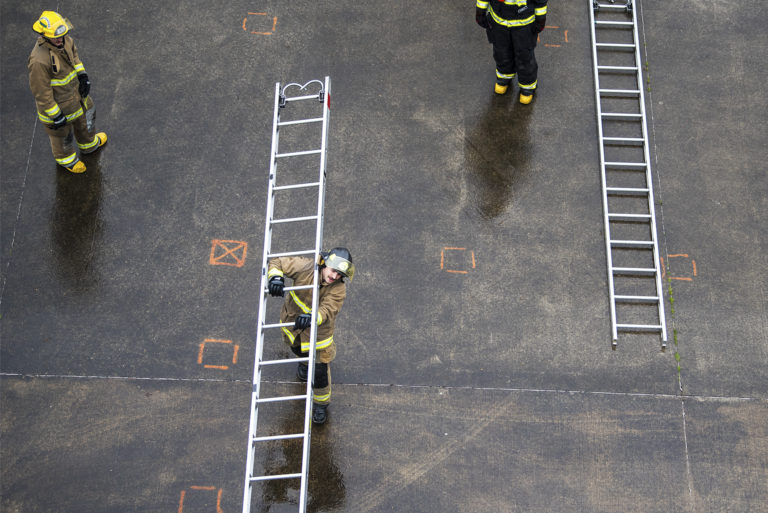 Instructor Graham Lasee, left, watches as recruit Skylar Daugherty with the Camas-Washougal Fire Department carries a ladder to a practice structure during training at Fire Station 42 on Wednesday afternoon, April 10, 2019.