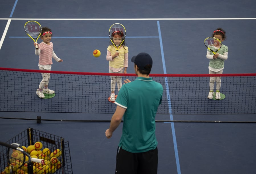 Fiona Chang, from left, and her triplet sisters, Amelia and Madeline, all 4 and of Camas, practice hitting over the net with their tennis instructor Stefan Lagielski during a lesson at Vancouver Tennis Center. The Changs are one of two sets of triplets who are taking lessons at the center.