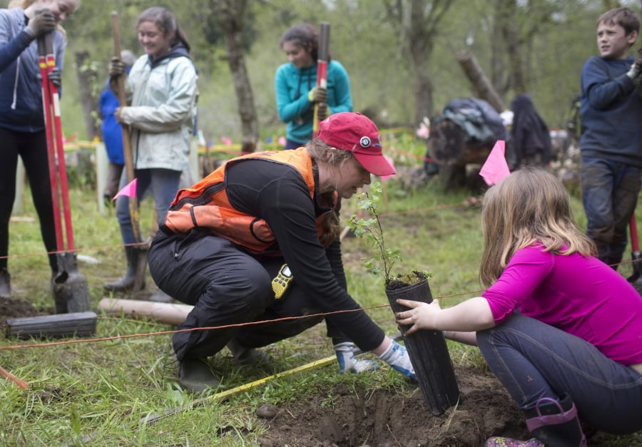Volunteer Emma Brenneman helps a girl plant a tree at an Earth Day event at Salmon Creek Regional Park in 2017.