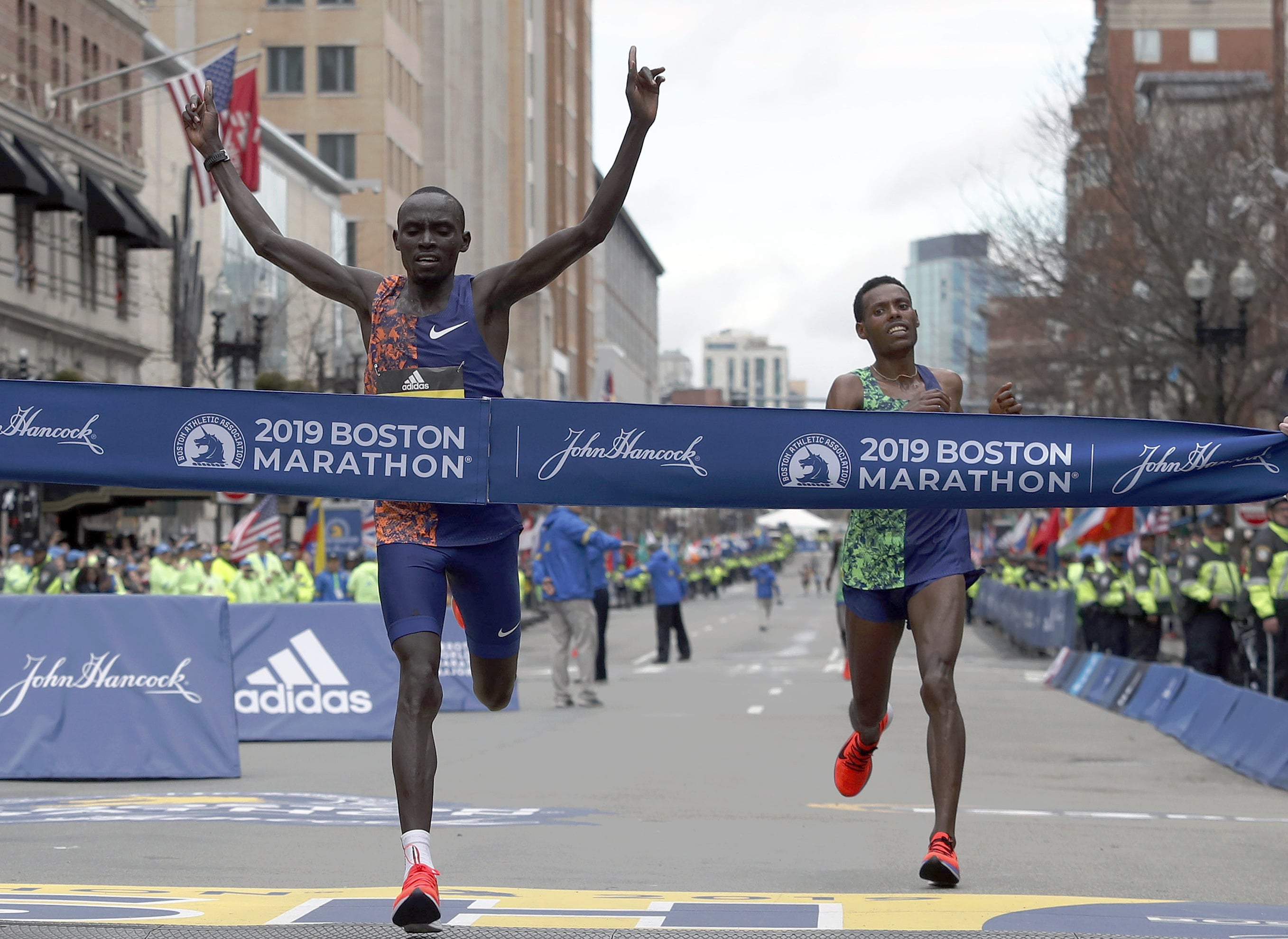 Lawrence Cherono, of Kenya, hits the tape to win the 123rd Boston Marathon in front of Lelisa Desisa, of Ethiopia, right, on Monday, April 15, 2019, in Boston.