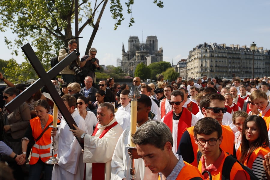 With Notre Dame cathedral in background, religious officials carry the cross during the Good Friday procession, Friday, April 19, 2019 in Paris.
