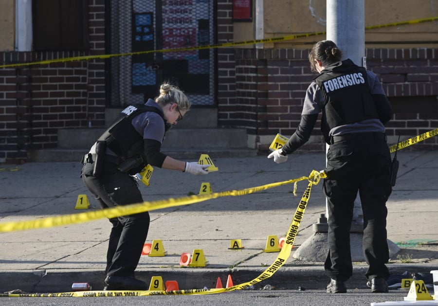 Baltimore police forensics officers place evidence markers next to bullet casings while investigating the scene of a shooting in Baltimore on Sunday, April 28, 2019. A gunman fired indiscriminately into a crowd that had gathered for Sunday afternoon cookouts along a west Baltimore street, killing one person and wounding seven others, authorities said. (Kenneth K.