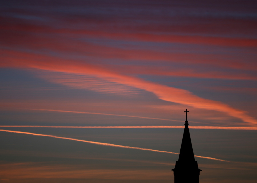 Contrails from jets glow pink as they are illuminated by the setting sun in the skies beyond a church in Kansas in 2014. According to a Gallup poll, the percentage of U.S. adults who belong to a church has fallen to a low of 50 percent last year.