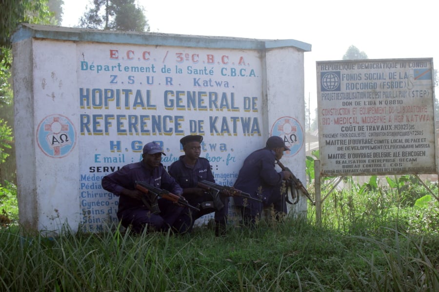Police shelter behind a hospital sign Saturday while they guard the facility in Butembo, Congo, after militia members attacked an Ebola treatment center in the city’s Katwa district overnight.