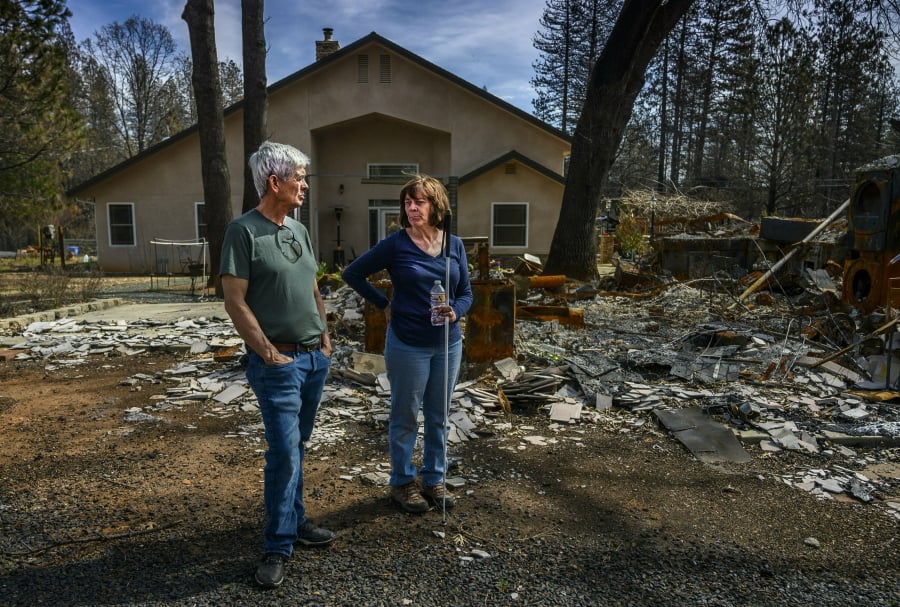 Oney and Donna Carrell stand March 19 near the ashes of her father’s house in Paradise, Calif. Their property had two homes on it before the fire, but the only one to survive (visible behind them) was built to fire-resistant standards that went into effect in 2008.