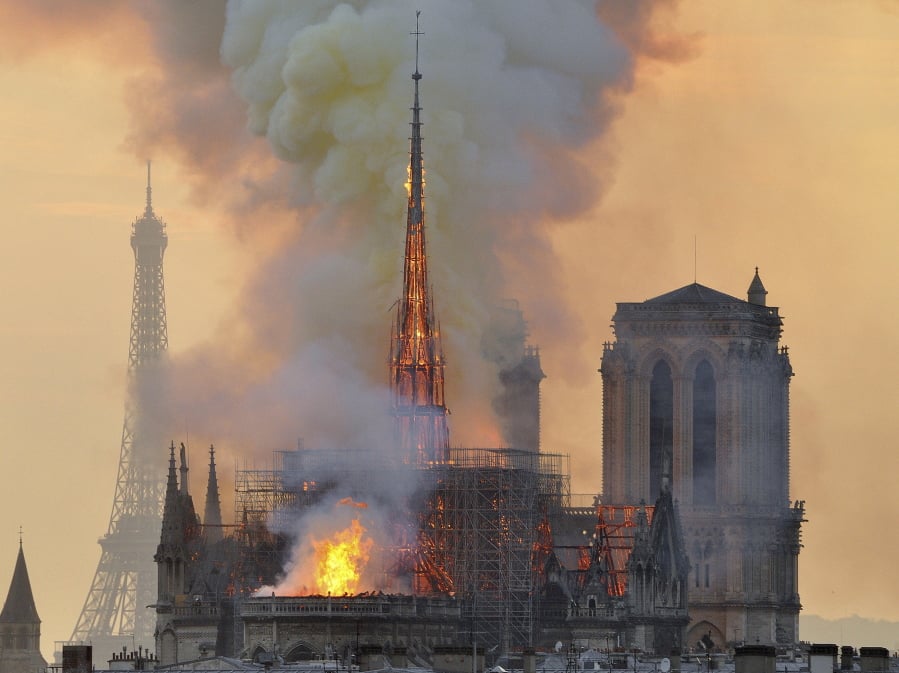 FILE - In this file photo dated Monday, April 15, 2019, with the Eiffel Tower behind, left, flames and smoke rise from the blaze at Notre Dame Cathedral in Paris that destroyed its spire and its roof but spared its twin medieval bell towers, and prompted a frantic rescue effort to save its most precious artefacts. The recent devastating Notre Dame fire in Paris was a warning bell that all of Europe needs to hear, since so many monuments and palaces across the continent are in need of better upkeep according to European officials. “We are so used to our outstanding cultural heritage in Europe that we tend to forget that it needs constant care and attention,” Tibor Navracsics, the European Union’s top culture official, told The Associated Press.