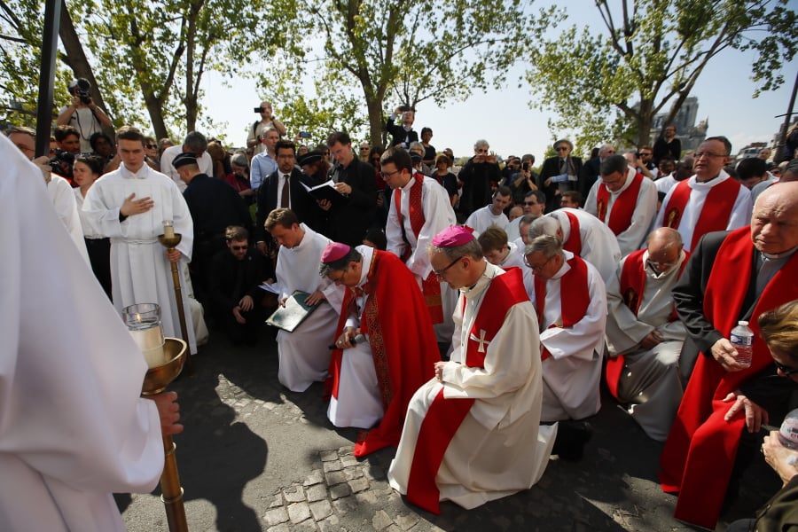 With Notre Dame cathedral, background right, religious officials pray during the Good Friday procession, Friday, April 19, 2019 in Paris.