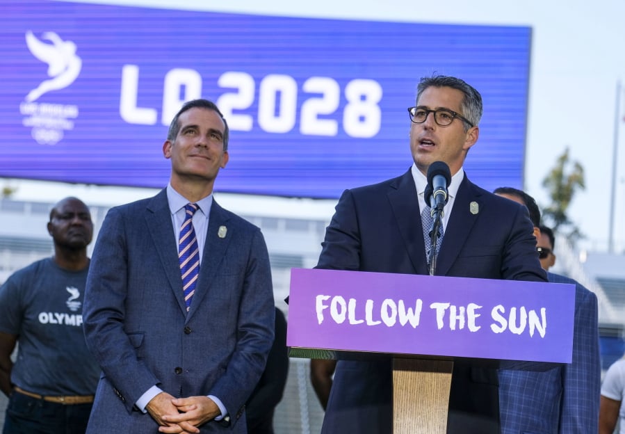 FILE - In this July 31, 2017, file photo, Los Angeles Mayor Eric Garcetti, left, listens as Los Angeles Olympic Committee leader Casey Wasserman speaks during a press conference to make an announcement for the city to host the Olympic Games and Paralympic Games 2028, at Stubhub Center in Carson, Calif. The price tag on the Los Angeles 2028 Olympics is now $6.88 billion, a $1.36 billion increase that comes mainly because of accounting measures designed to better reflect inflation over the long lead-up to those games. Most key numbers the organizing committee released Tuesday, April 30, 2019, are essentially the same as those submitted in the original bid documents, only adjusted from 2016 dollars to reflect the real value of the dollars at the time they’ll be received or spent. (AP Photo/Ringo H.W.